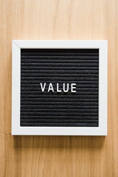 A black felt board reading 'VALUE' framed in white, set against a wooden backdrop. Ideal for business concepts.